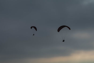 Low angle view of people paragliding against sky