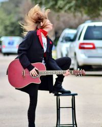 Woman playing guitar while standing on road in city