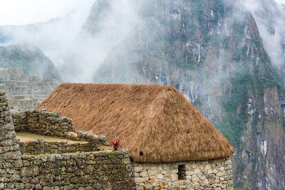 Thatched roof house against rocky mountains during foggy weather at machu picchu
