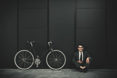 Portrait of young man sitting on bicycle against wall