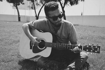 Young man playing guitar while smoking cigarette at park