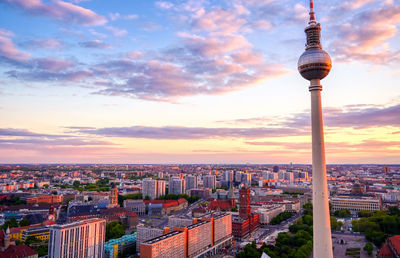 Communications tower in city against sky during sunset