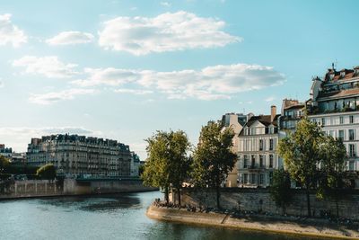 Parisian buildings in city against cloudy sky and seine river