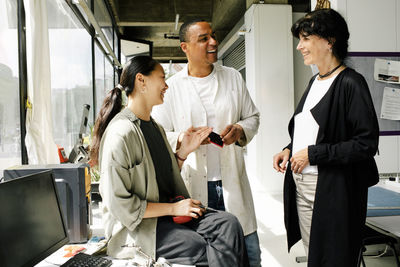 Smiling male and female technicians discussing with mature customer at workshop