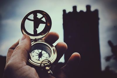 Close-up of hand holding clock against sky