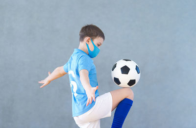 Side view of boy wearing mask playing with soccer ball