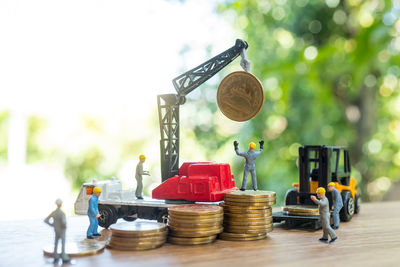 Close-up of figurines with toy crane and forklift with coins on table