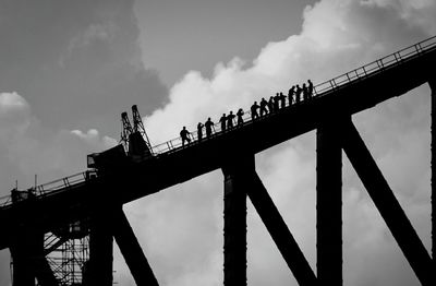 Low angle view of silhouette bridge against sky and people climbing on it. 
