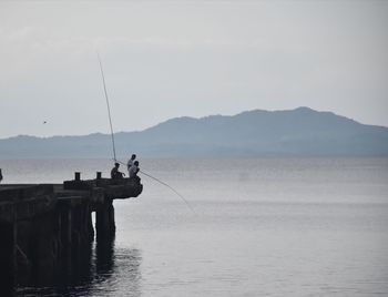 Man fishing in sea against sky