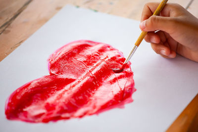 Cropped hand of child painting red heat shape on white paper