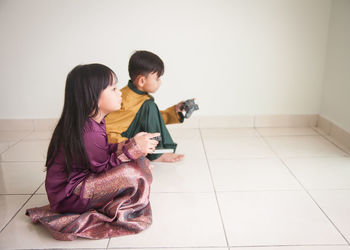 Siblings playing video game while sitting on floor at home