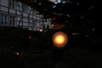 Close-up of illuminated lighting equipment on field against sky at night