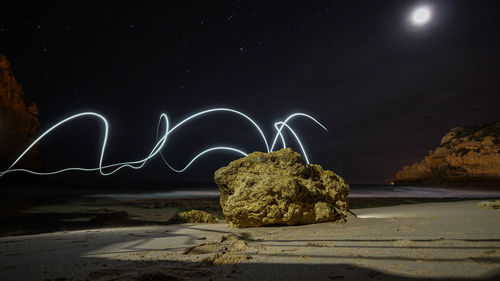 Rock at beach with illuminated light painting in sky at night