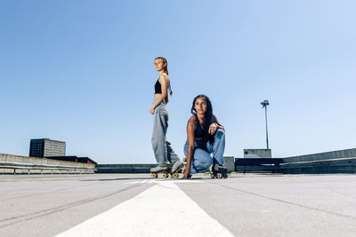 Two girls roller skating on an outdoor car park