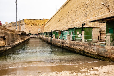 Canal by old building against sky