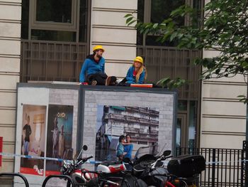 Man and woman sitting on bicycle against building in city