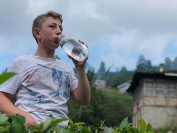 Low angel view of man drinking water while standing against sky