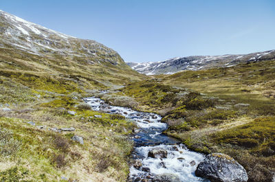 Scenic view of stream by mountains against clear sky