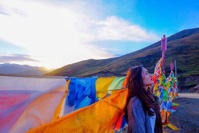 Side view of thoughtful young woman standing by colorful prayer flags on field