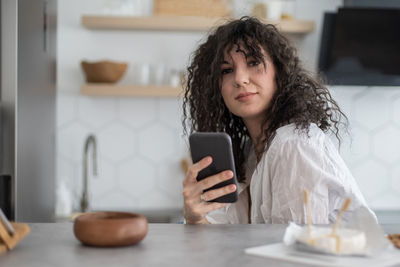 Portrait of smiling woman holding mobile phone at home