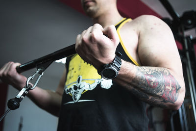 Midsection of young man using pulley in gym