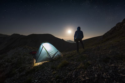 Rear view of silhouette man camping on mountain at night