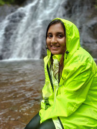 Portrait of young woman standing against waterfall