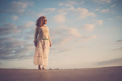 Woman standing at beach against sky during sunset