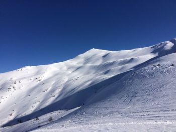 Low angle view of snowcapped mountains against clear blue sky