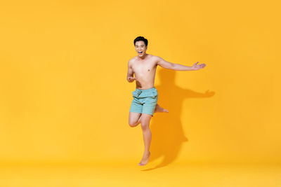 Portrait of shirtless man standing against yellow background