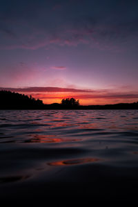 A tranquil lake mirrors a vibrant red sunset in småland. ideal for nature and travel projects.