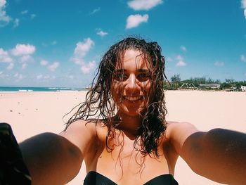 Portrait of smiling woman standing at beach against blue sky during sunny day