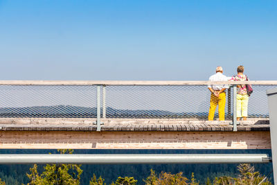 Rear view of people standing by railing against sea