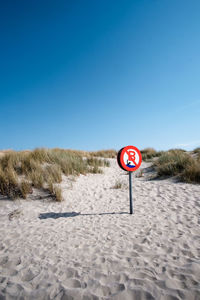 Road sign on sand against clear sky