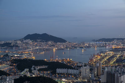 High angle view of illuminated city by sea against sky