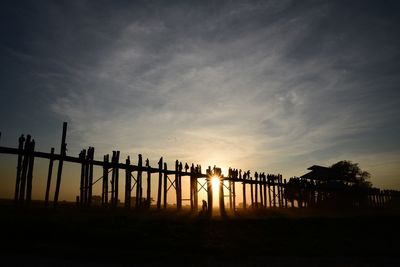 Silhouette people walking on footbridge against sky during sunset