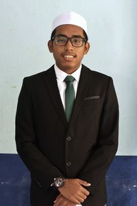 Portrait of young man wearing suit standing against wall