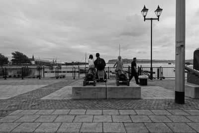 People sitting on sidewalk in city against sky