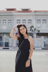 Portrait of young woman standing against building in city