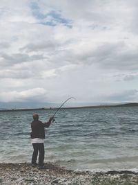 Rear view of man fishing in sea against sky