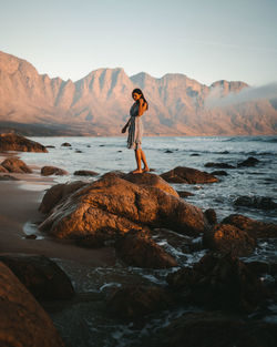 Woman standing on rock by sea against sky