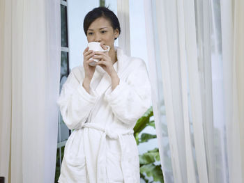 Woman drinking coffee while leaning on window