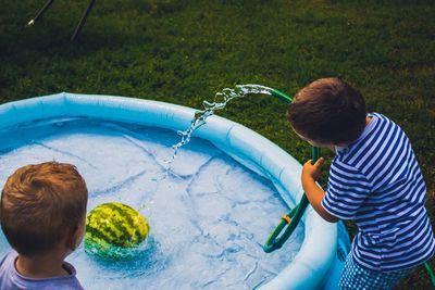 Rear view of boys filling wading pool with water