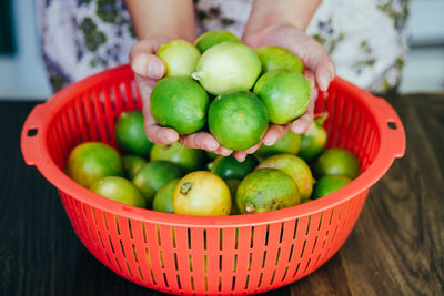 Midsection of person holding fruits in basket on table