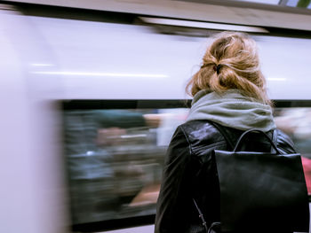 Rear view of woman standing against blur metro train at subway station