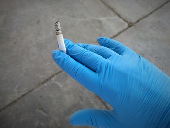 Cropped hand holding cigarette against footpath