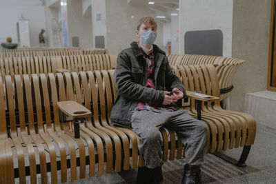 A man travels during a pandemic in a medical mask, sits while waiting for a trip, at a train station