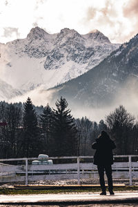 Rear view of man standing on snowcapped mountain against sky
