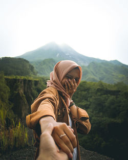 Cropped image of man holding woman hand against mountain ranges and sky