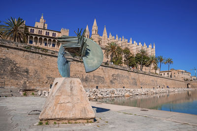 Statue on promenade by canal against medieval la seu cathedral